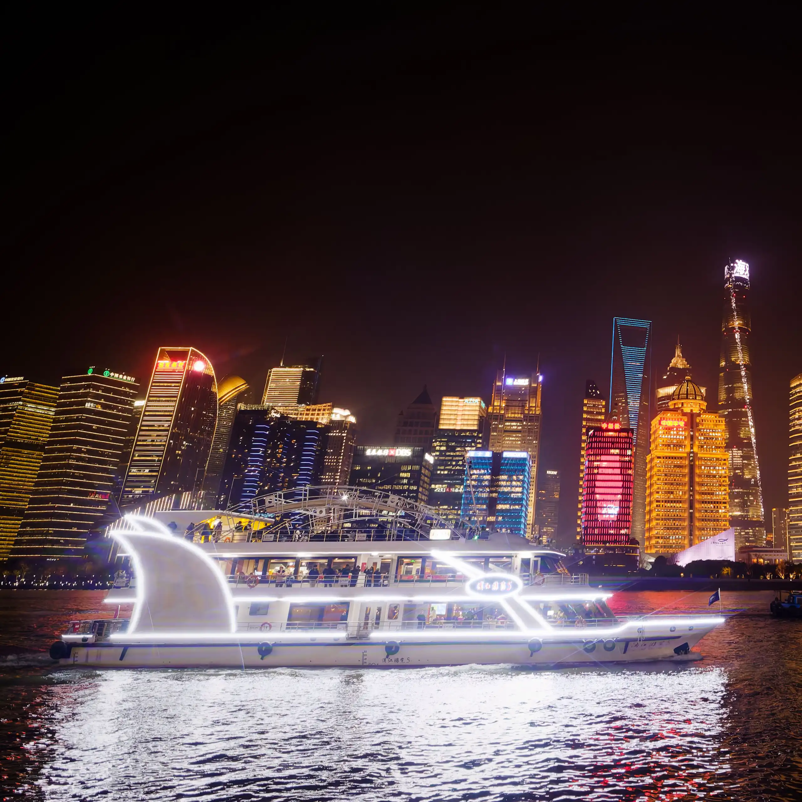 A boat with Shanghai skyline behind lit up at night.