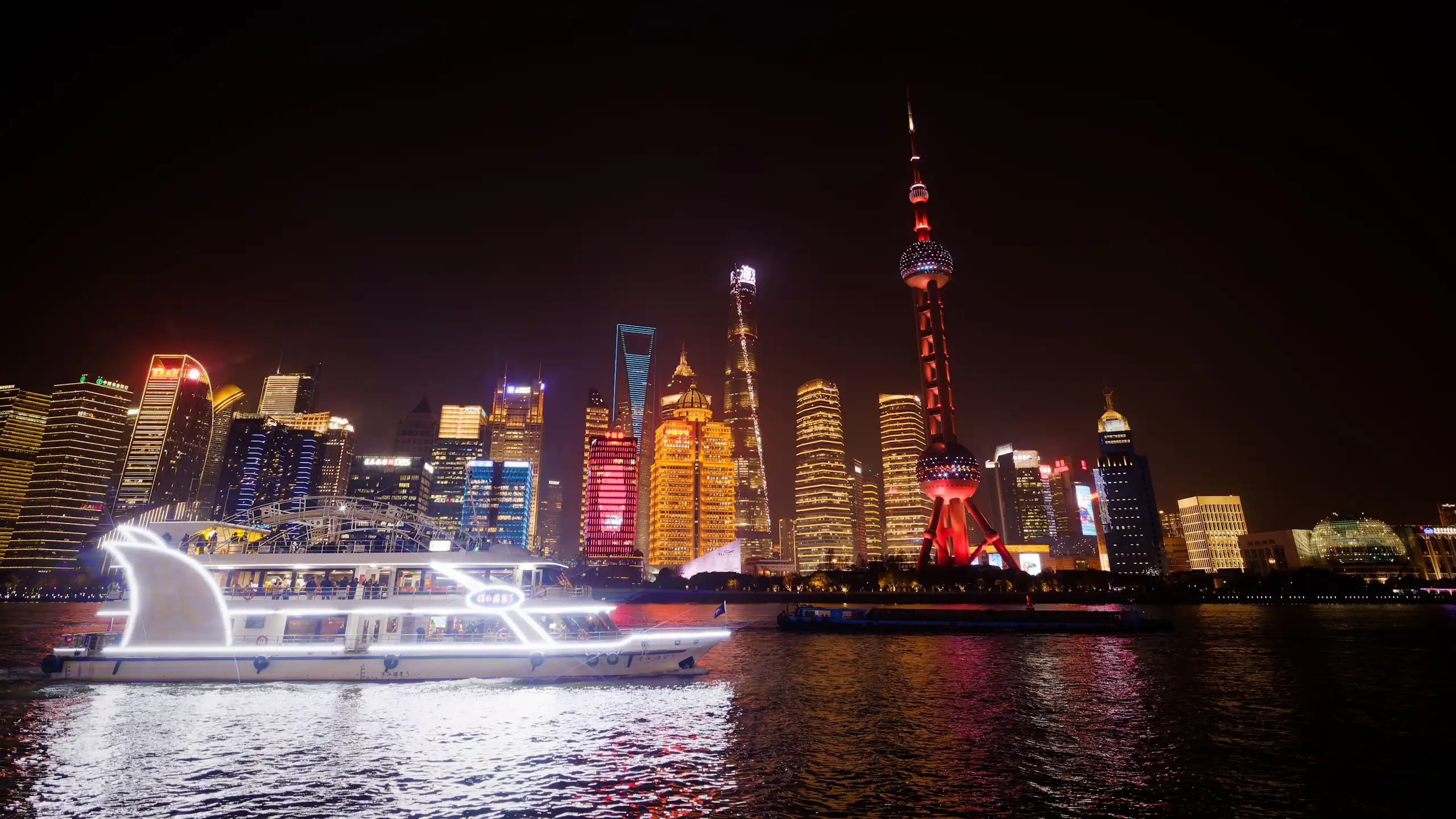 A boat with Shanghai skyline behind lit up at night.