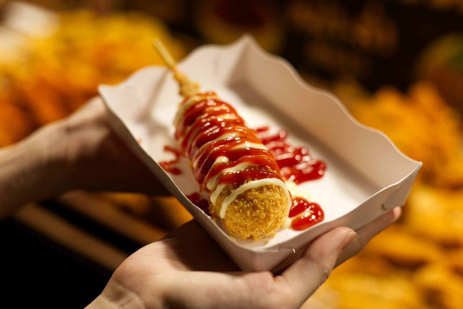 Une personne tient dans ses mains une barquette remplie d'un corn dog.
