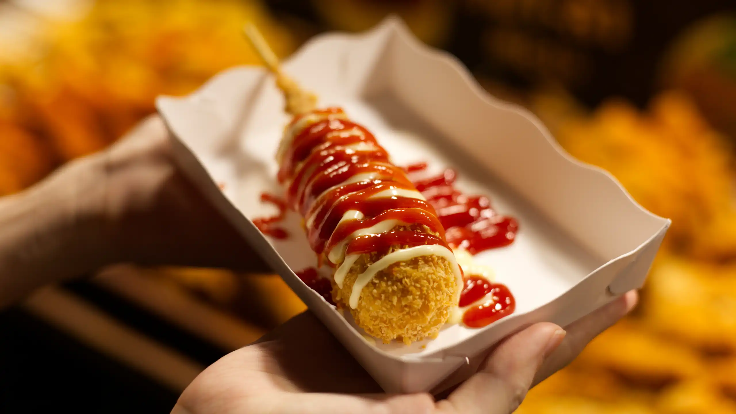 Une personne tient dans ses mains une barquette remplie d'un corn dog.
