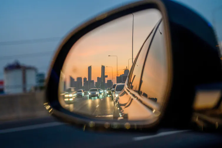 Close-up of side view mirror reflecting city skyline and other cars on the road