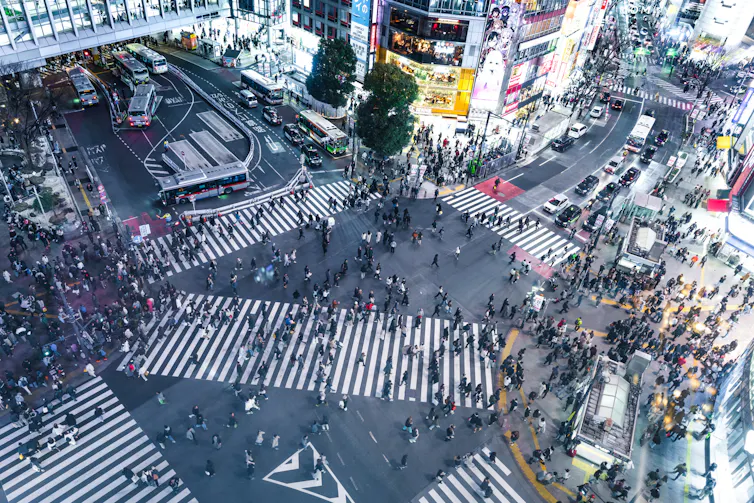 Aerial view of a busy intersection in a city, crowds of people milling about and buildings lit with animated billboards