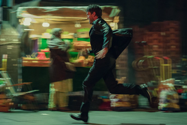 A man running at speed along a market street at night.