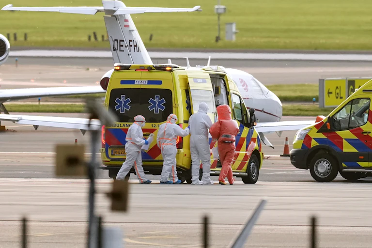 Du personnel médical est agglutiné devant un véhicule d'urgence sur une piste d'atterrissage