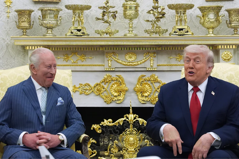 Two older men sit in a garishly gilded office.