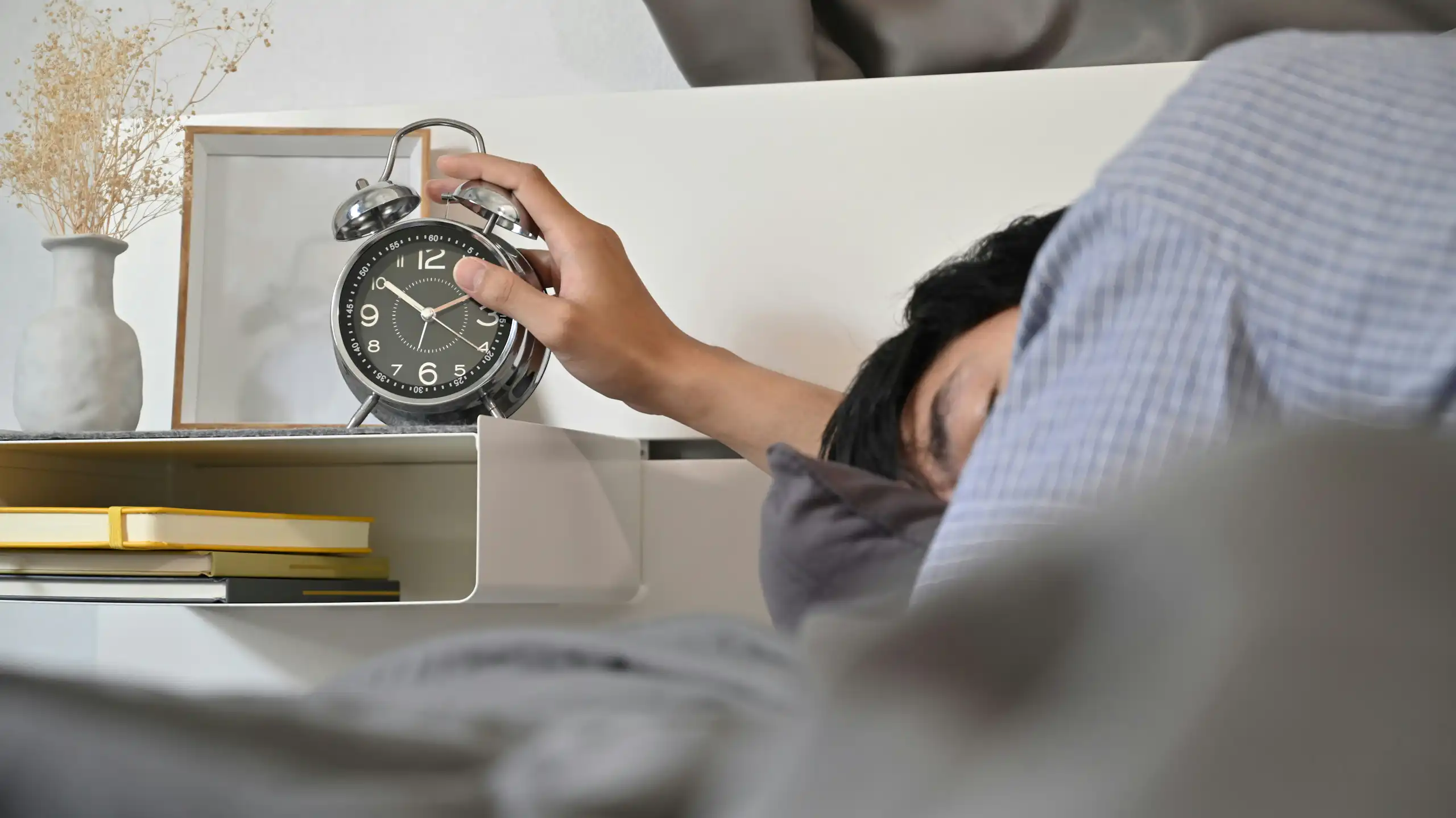 A person turning off an alarm clock from bed