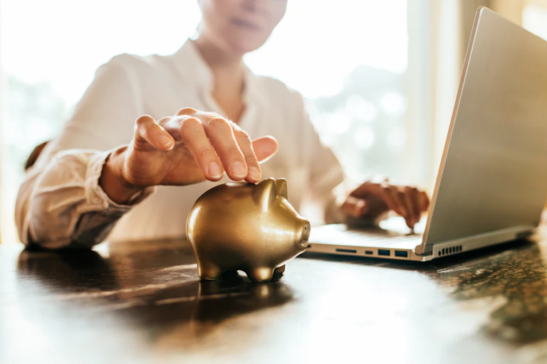 A woman working at a laptop with a golden piggybank beside her