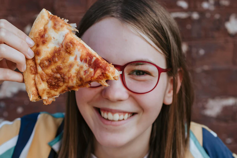 A happy teenager holding a pizza slice.