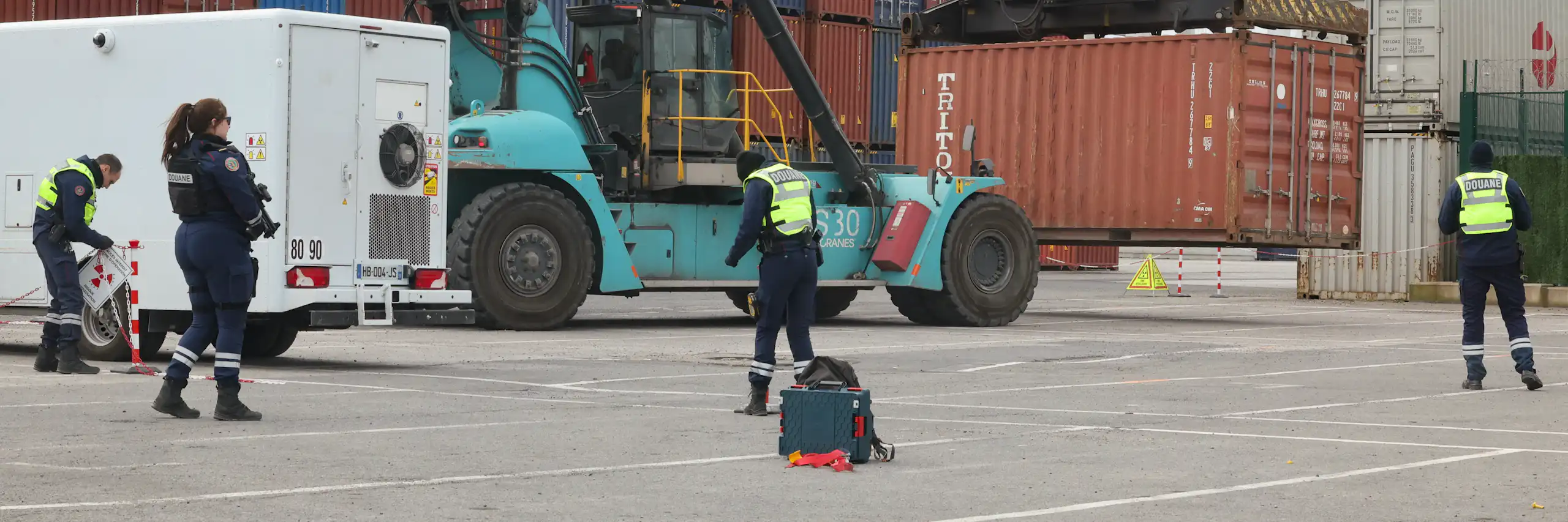 Sur les docks de Dunkerque, des douaniers inspectent un conteneur.