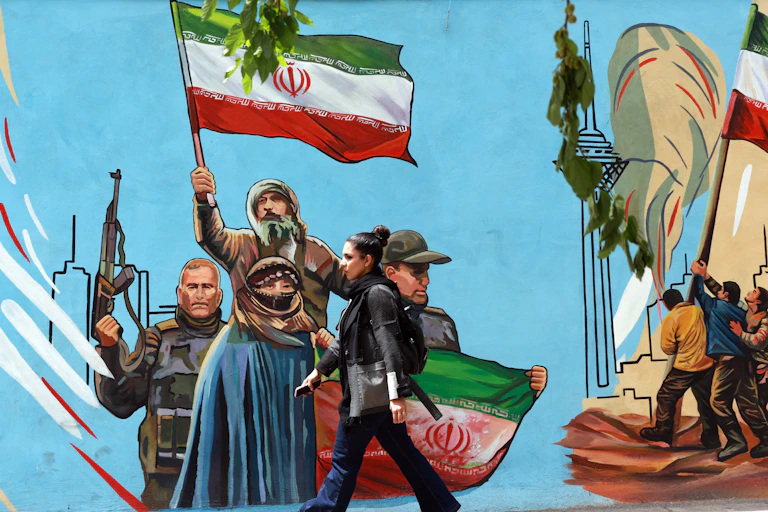 A woman walks next to a mural painted on a wall in Tehran depicting Iranians holding their country's national flag.