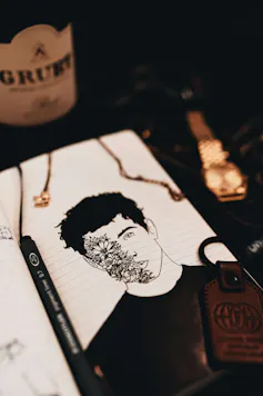 Dibujo de una persona con hojas que cubren la mitad de su rostro, con un lápiz dejado en una libreta.