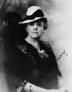 Escribir para siempre: cómo podría ser una nueva forma de aprender a escribir y resistir la IA 1 Fotografía en blanco y negro de una mujer con sombrero, gafas redondas y vestido de principios del siglo XX con escote en pico, lazo y manga 3/4 con bordado de follaje/arabescos.