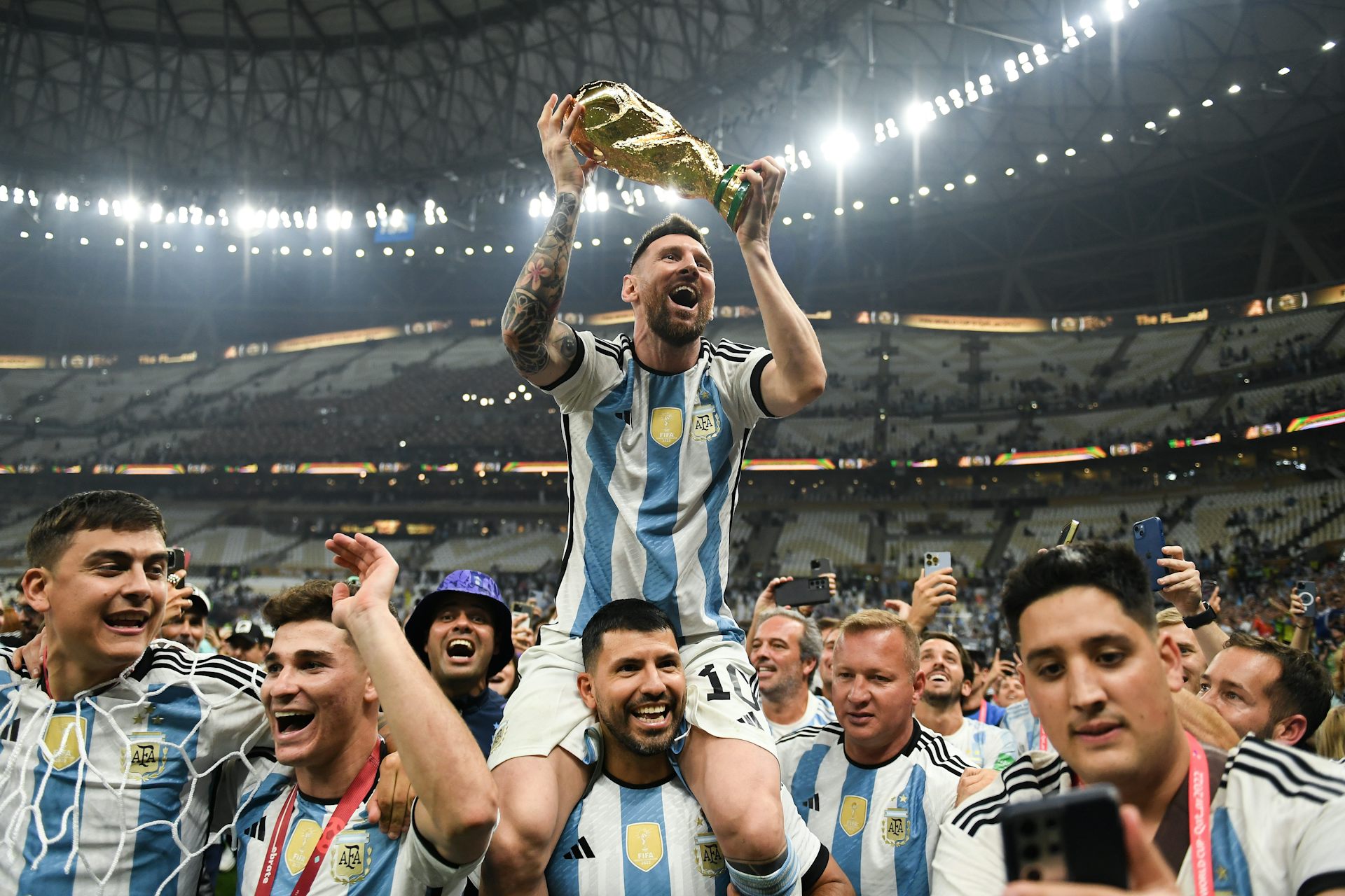 A man in a blue and white jersey holds aloft a gold trophy.