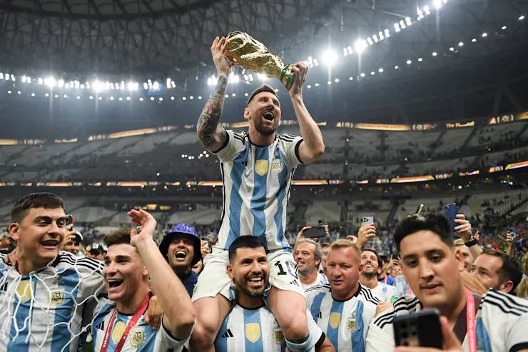 A man in a blue and white jersey holds aloft a gold trophy.