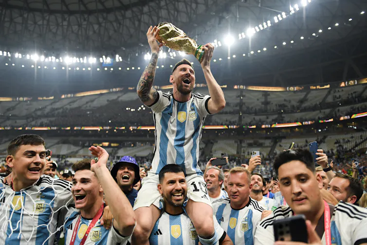 A man in a blue and white jersey holds aloft a gold trophy.
