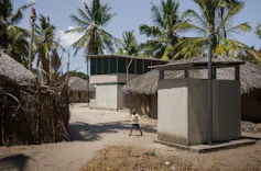 A double storey home next to some homes made of grass