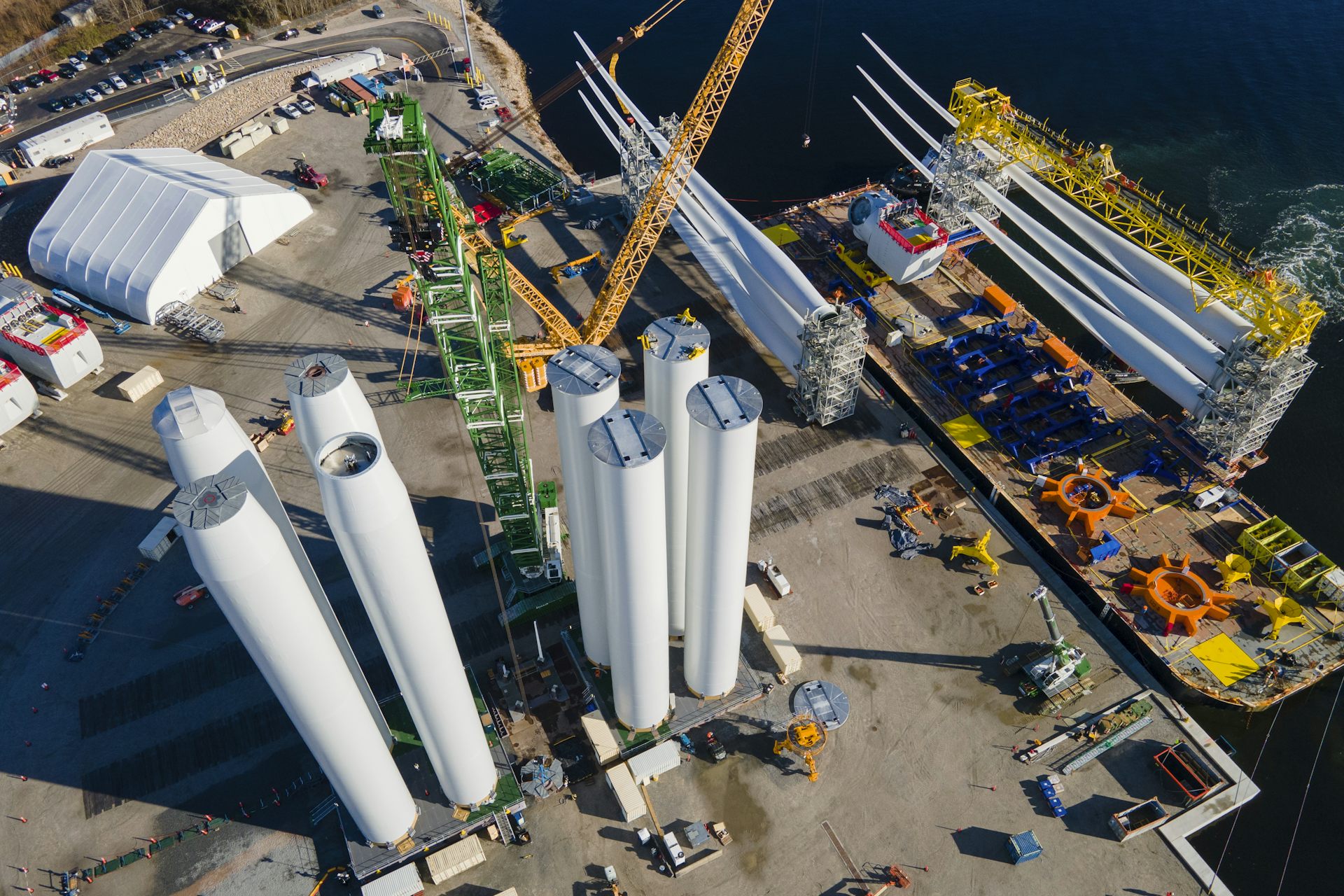 An aerial view of a port showing the towers of future wind turbines and blades in a rack on a ship nearby.
