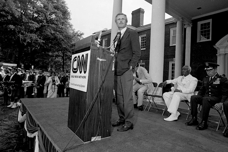 A man in a black and white photo stands at a lectern outdoors.