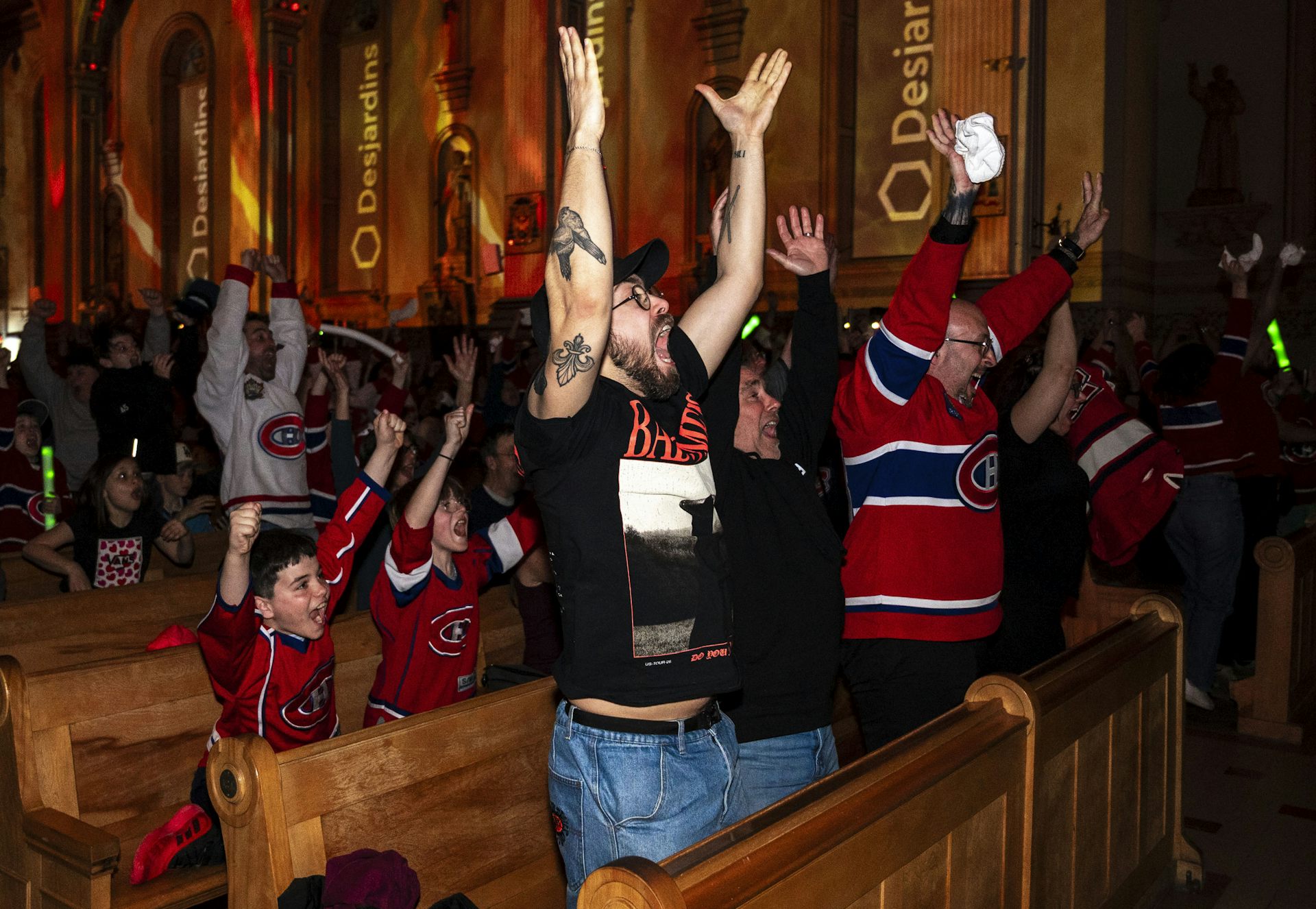 Fans in hockey jerseys seated in church pew stand and cheer