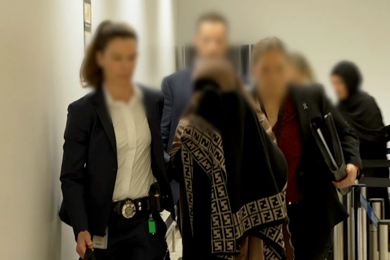 A woman in a burqa is flanked either side by female police officers with their faces blurred out