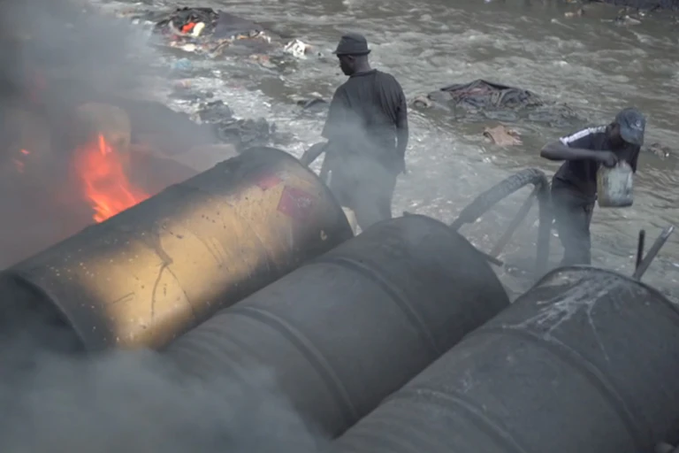 Flames visible under large metal drums being tended by two people
