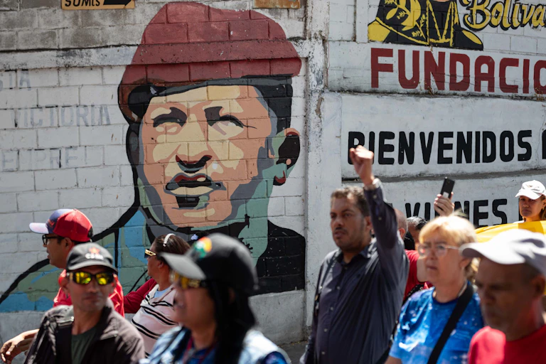 Venezuelans walk past a mural depicting Hugo Chávez.
