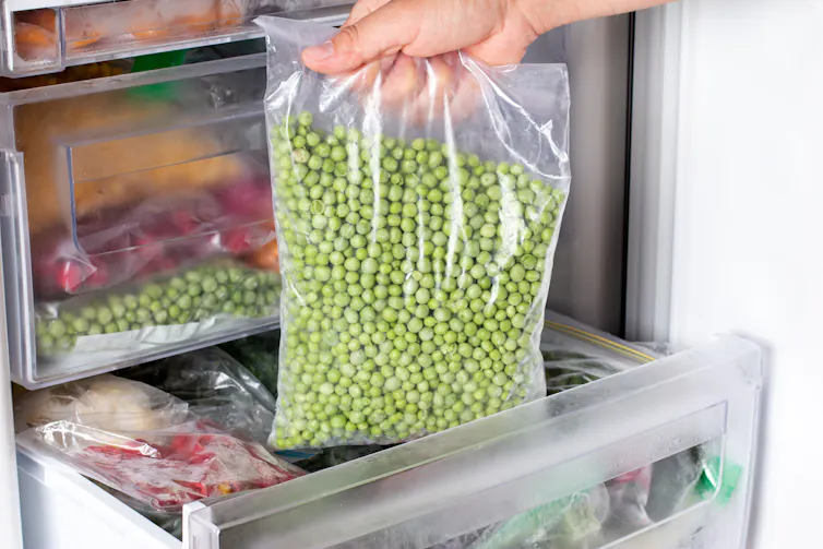 A person's hand pulls out a bag of peas from the freezer.