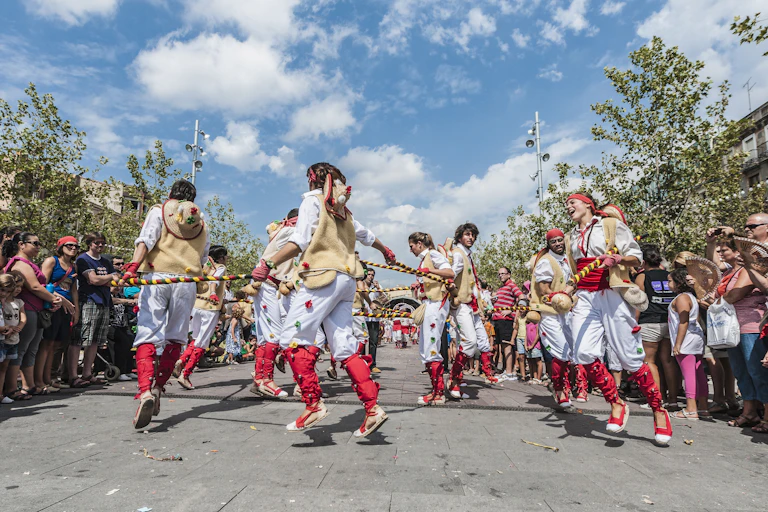 Homes i dones vestits amb pantalons blancs i complements rojos ballen en cercle, al carrer.