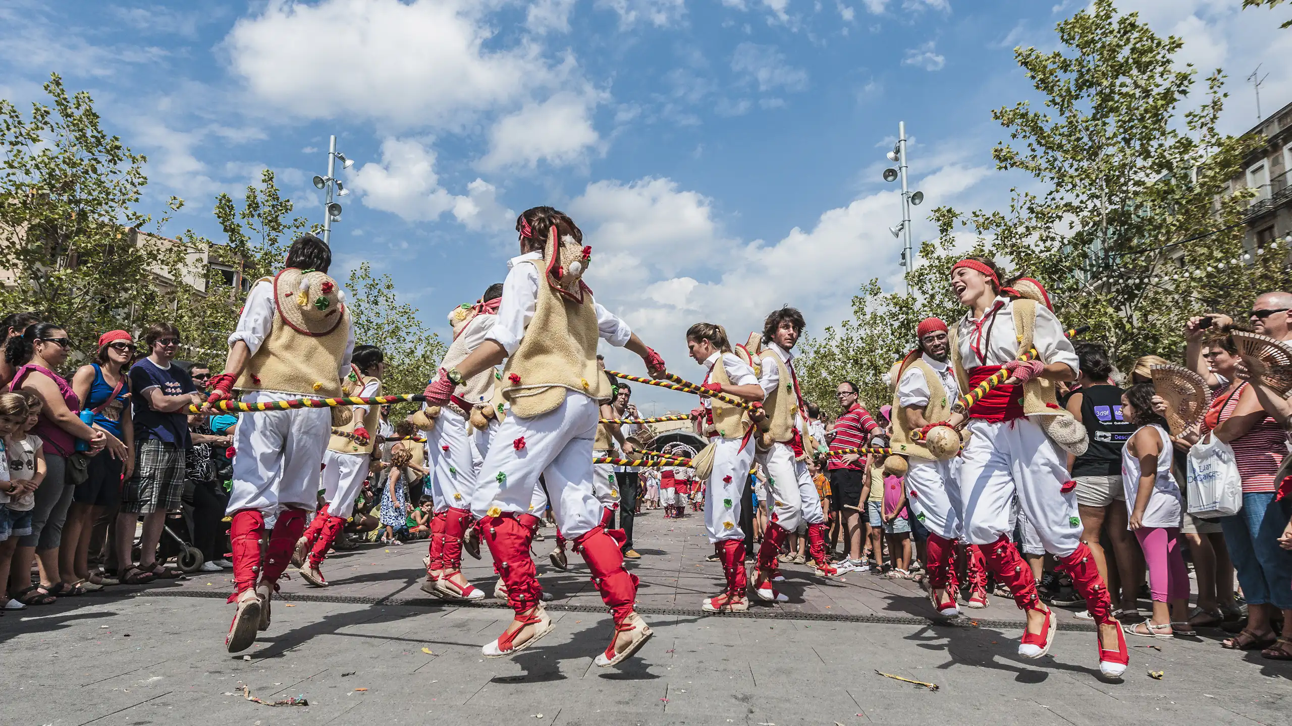 Homes i dones vestits amb pantalons blancs i complements rojos ballen en cercle, al carrer.