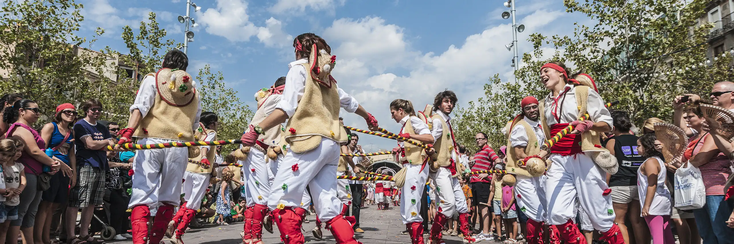 Homes i dones vestits amb pantalons blancs i complements rojos ballen en cercle, al carrer.