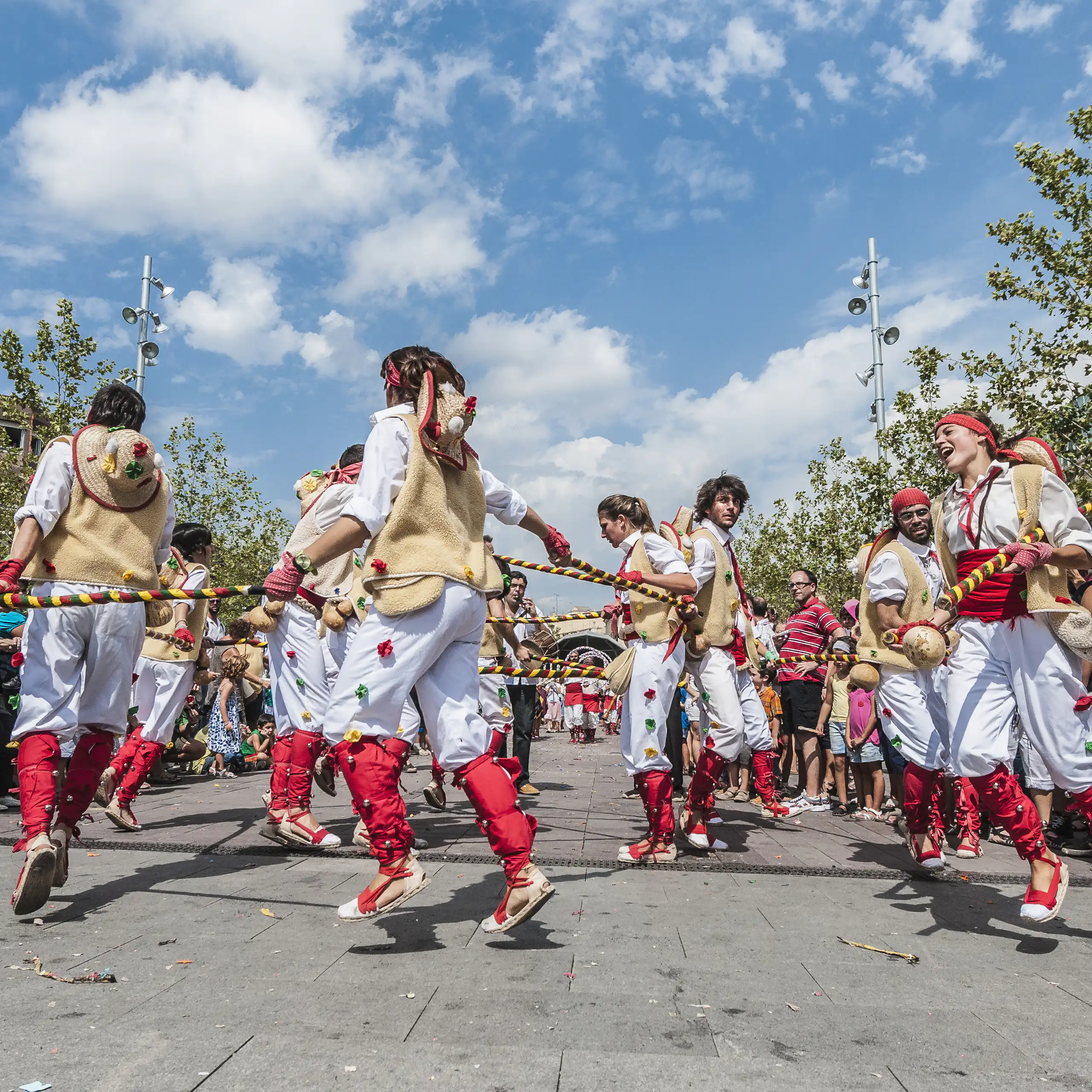 Homes i dones vestits amb pantalons blancs i complements rojos ballen en cercle, al carrer.