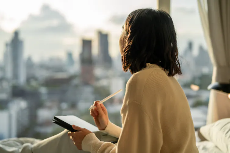 Young woman looks out window holding tablet and pen