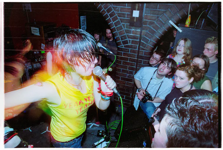 Woman in yellow tshirt performing to a sweaty crowd