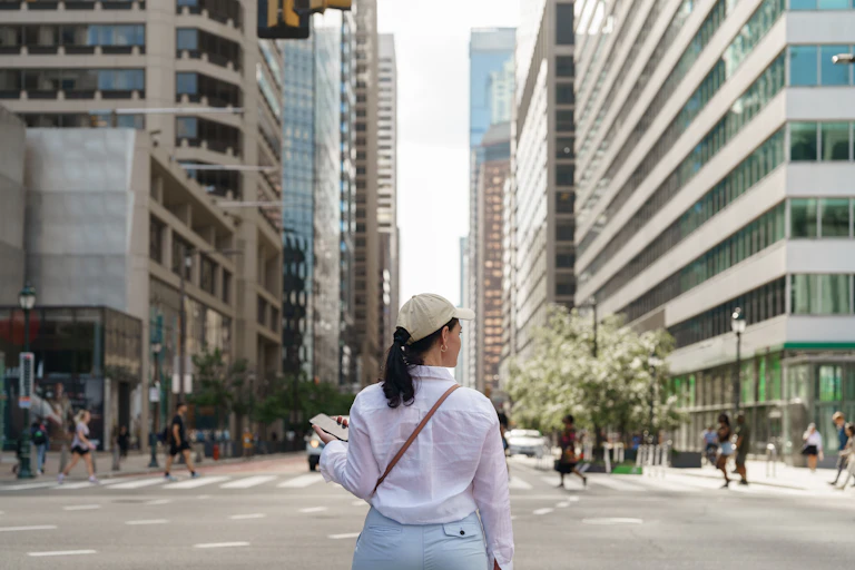 Woman in baseball cap holds phone while looking across large intersection