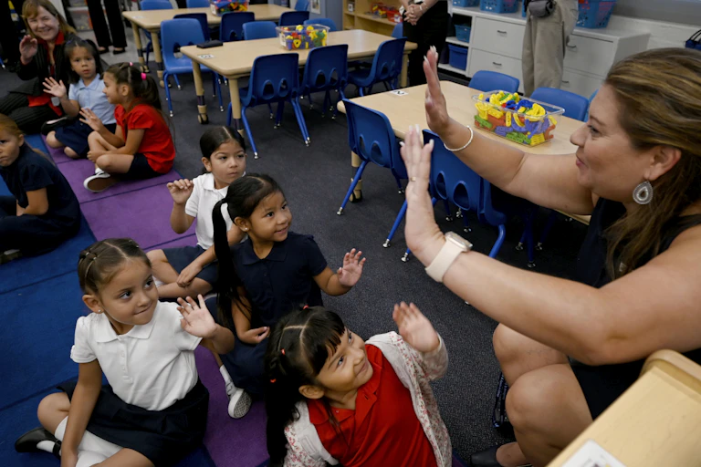 A woman holds up her hands in a high five, as a group of young children look and smile at her.