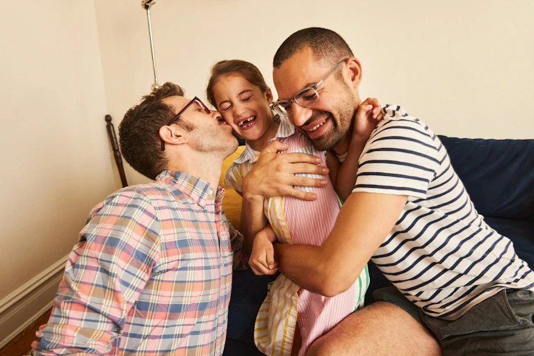 A male couple embrace a child between them on a couch.