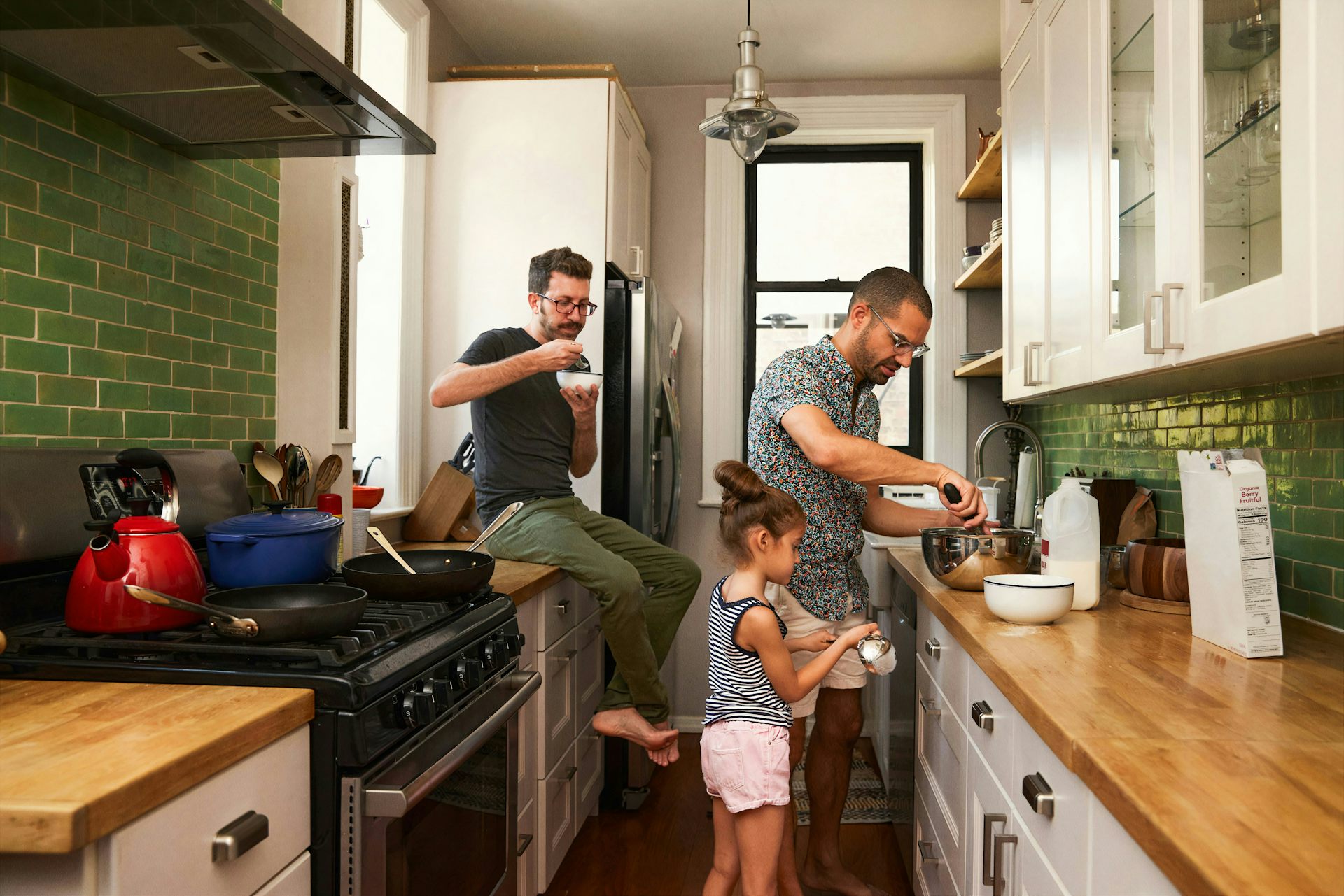 Una pareja de hombres cocina con un niño en la cocina.