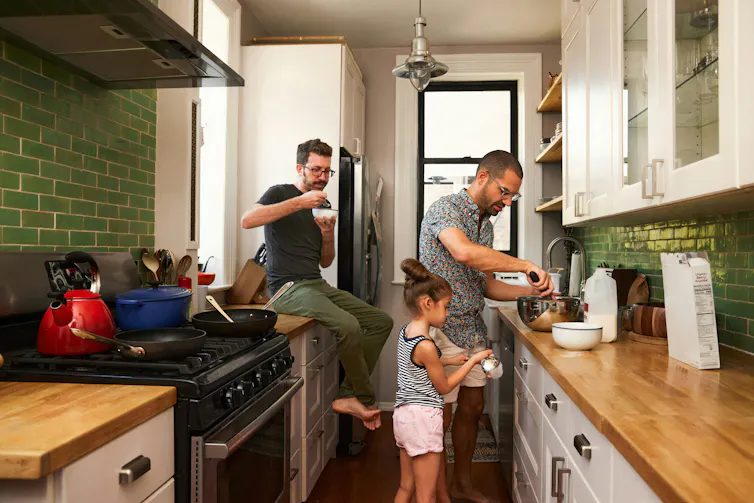 A male couple in the kitchen cooking with a child.