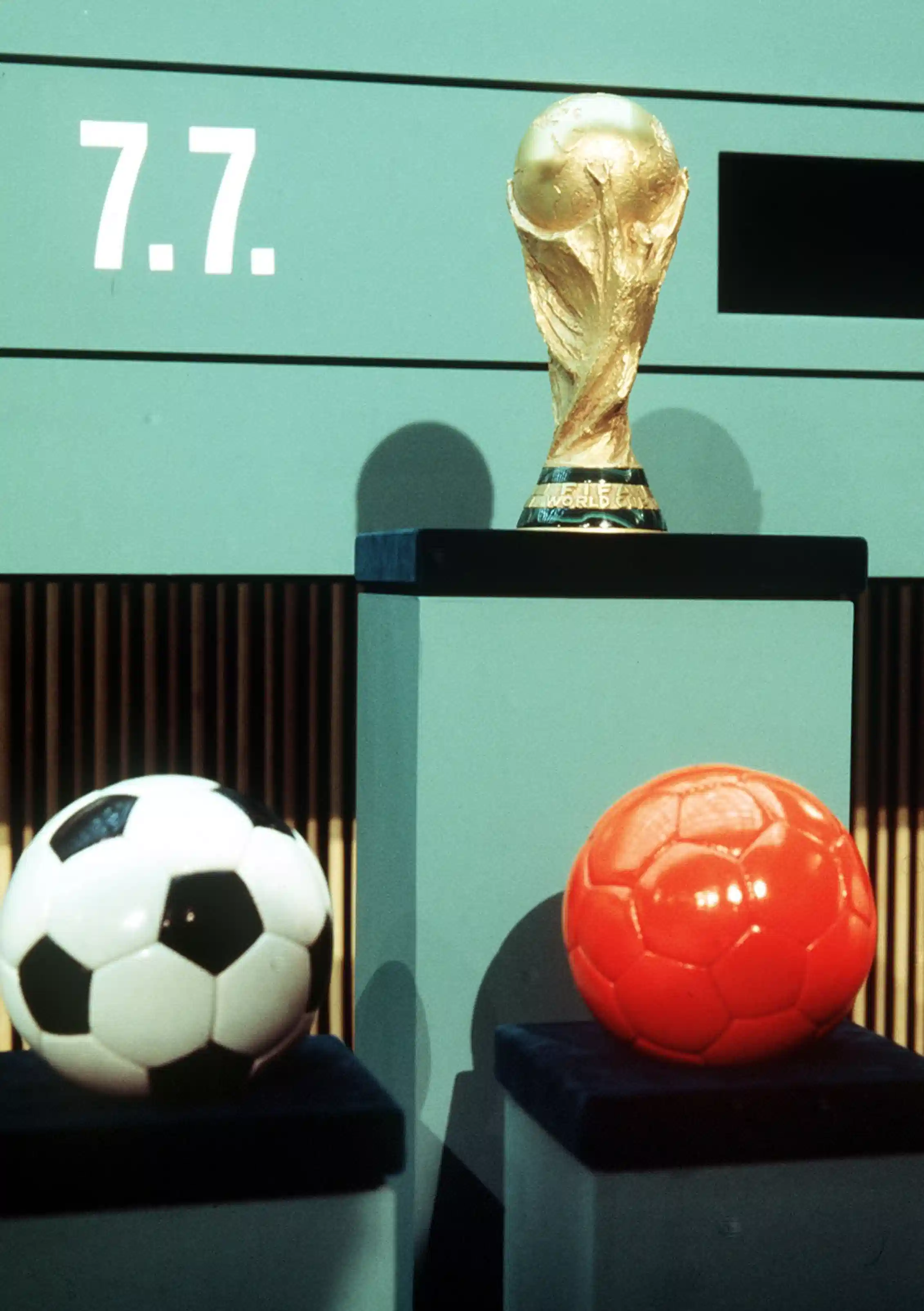 An orange ball and a black and white ball are under a trophy.