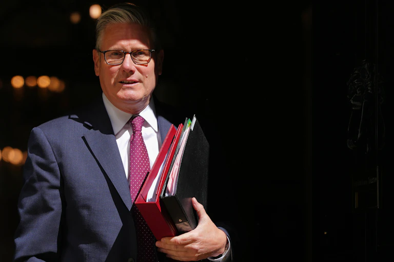 Keir Starmer in half shadow, holding files.