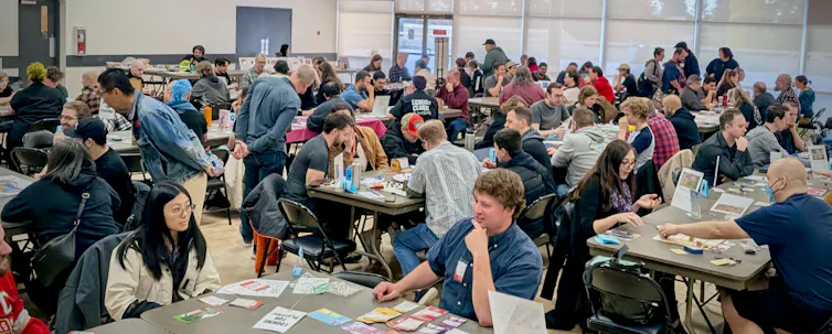 a large room with people seated at tables playing various board games