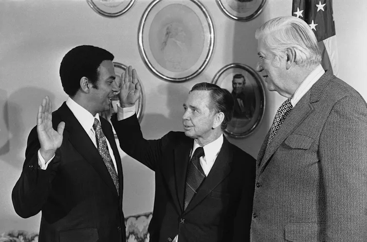 Three men in suits with the one on the left, who is Black, swearing an oath with his right hand raised.