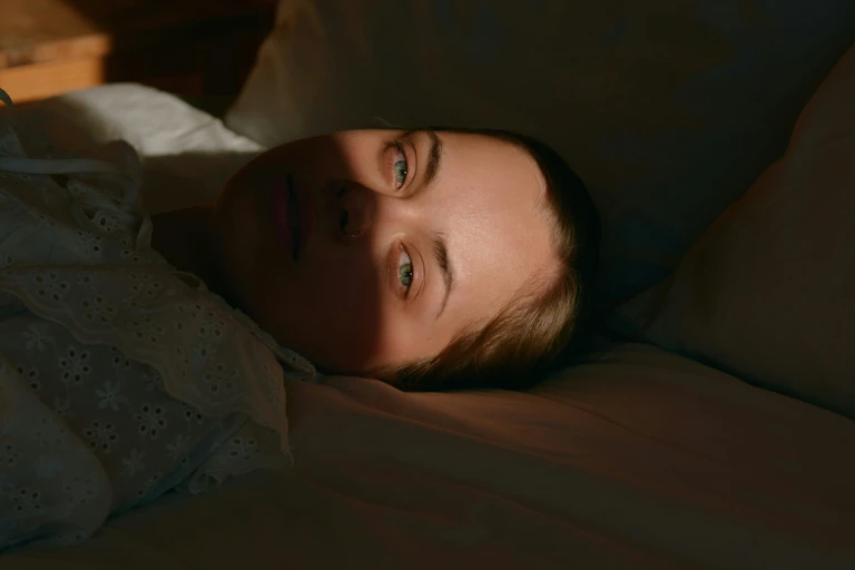A woman lying awake in bed half in shadow