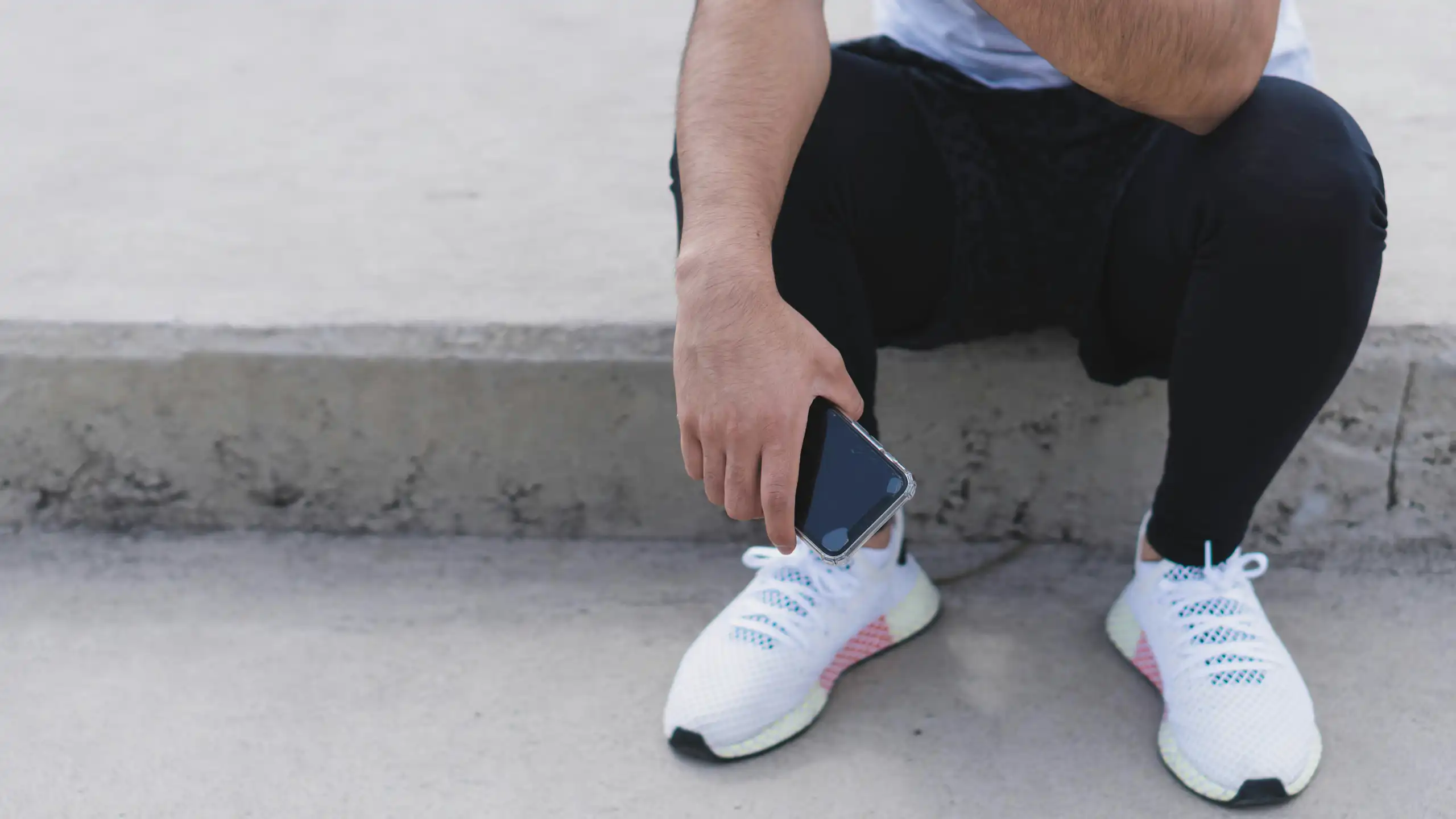 A man in running sneakers and attire holds their phone while sitting down.
