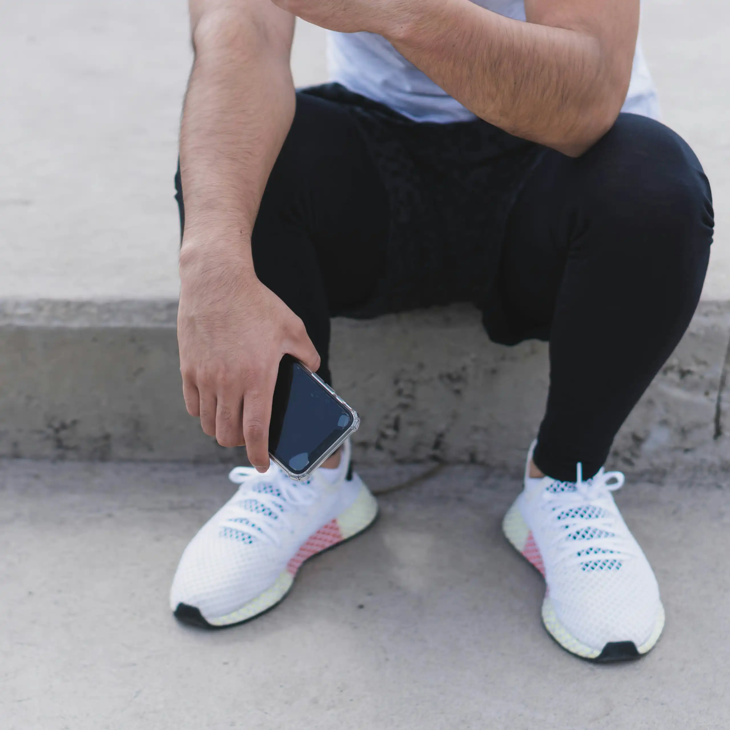 A man in running sneakers and attire holds their phone while sitting down.