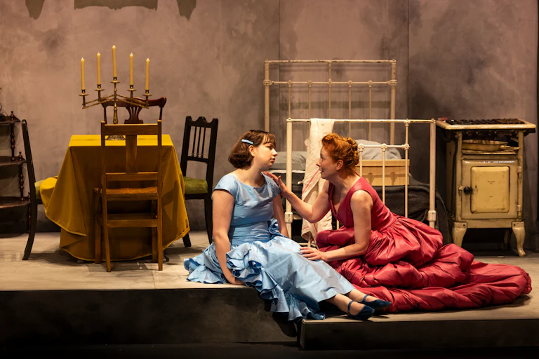 Production image: a mother and daughter sit on the floor in brilliant ball gowns.