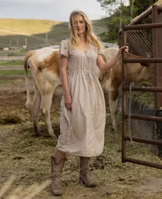 a blonde woman in a dress and cowboy boots, with cows