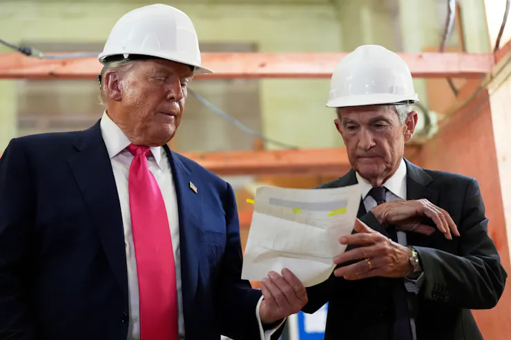 Wearing safety helmets, Jerome Powell and Donald Trump look over a document of construction cost figures during a visit to the Federal Reserve headquarters on July 24, 2025.
