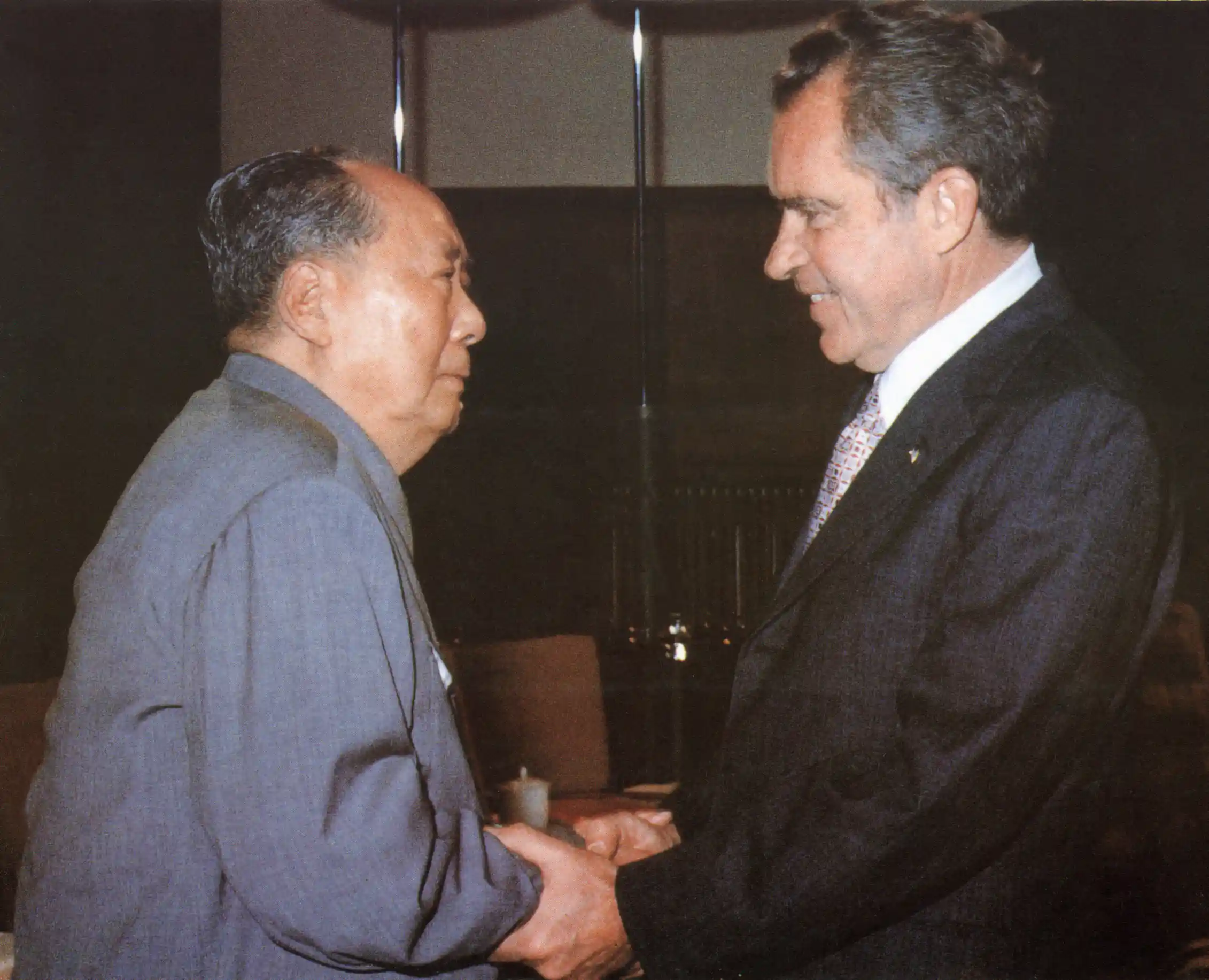 Two men in suits shake hands.