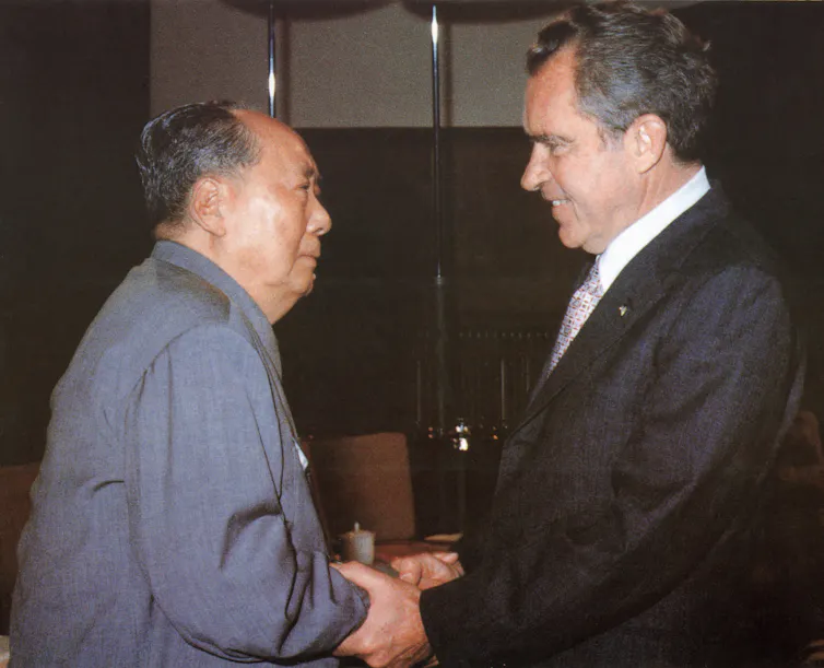 Two men in suits shake hands.